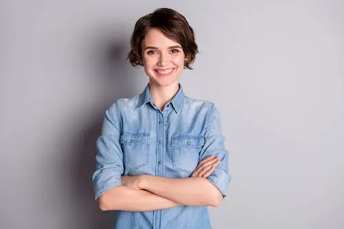 An image of a women with chin-length brunette hair wearing a light jean shirt smiling at the camera. The background is light blue.  The woman is not a complete representation of the person writing the testimonial.